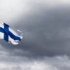 The Finnish flag waves proudly against a dramatic, cloudy sky, symbolizing national identity.