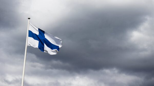 The Finnish flag waves proudly against a dramatic, cloudy sky, symbolizing national identity.