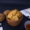 Crispy potato chips in a rustic wooden bowl with seasoning and potatoes nearby.