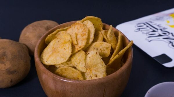 Crispy potato chips in a rustic wooden bowl with seasoning and potatoes nearby.