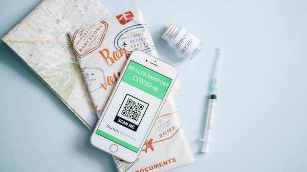 Flat lay of a COVID-19 health passport on a smartphone with vaccine, syringe, and travel documents.
