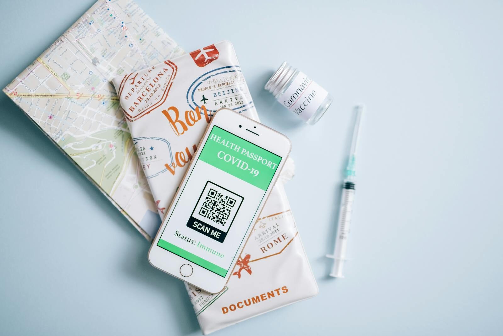 Flat lay of a COVID-19 health passport on a smartphone with vaccine, syringe, and travel documents.