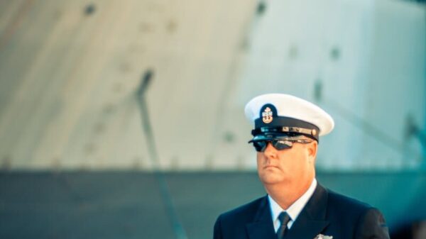 A US Navy officer in dress uniform standing on a ship's deck, representing military professionalism.