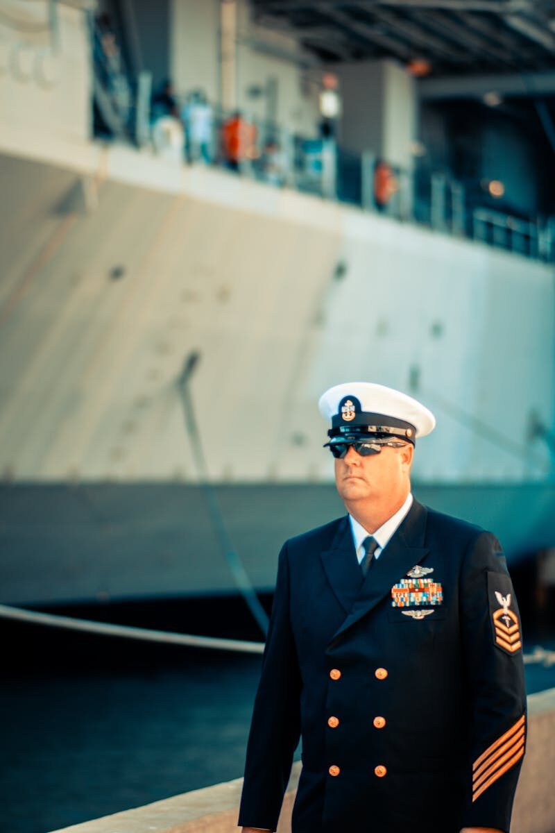 A US Navy officer in dress uniform standing on a ship's deck, representing military professionalism.