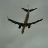 A commercial airplane approaching for landing against a backdrop of cloudy skies, seen from below.
