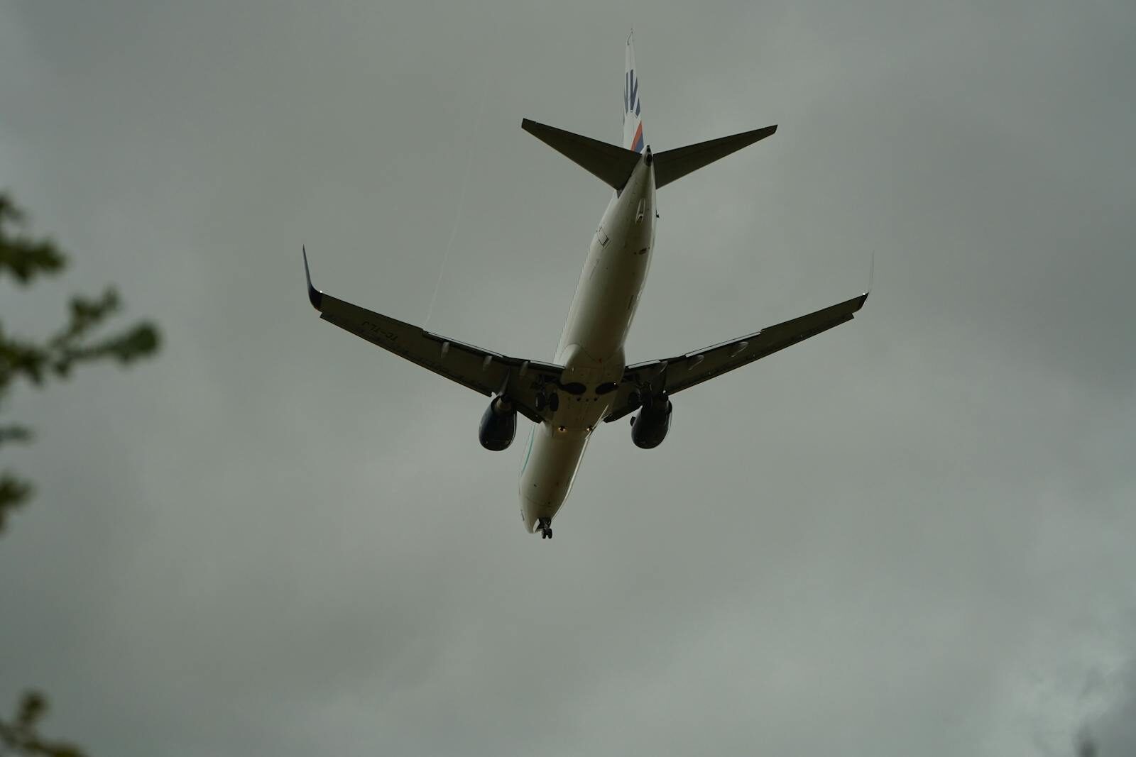 A commercial airplane approaching for landing against a backdrop of cloudy skies, seen from below.