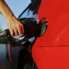 Close-up of a person refueling a red car at an outdoor gas station during the day.