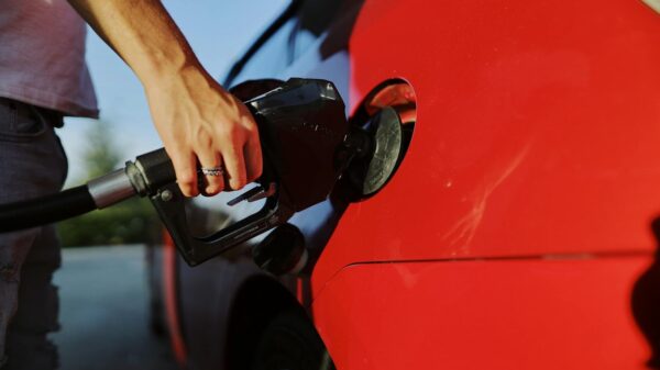 Close-up of a person refueling a red car at an outdoor gas station during the day.