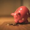 A red ceramic piggy bank with polka dots surrounded by coins, symbolizing savings and finance.