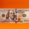 Detailed photo of a 100 dollar bill against a vibrant orange background, perfect for finance themes.
