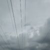 From below power line with poles and wires against gray cloudy sky at dusk
