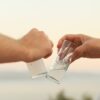 Two hands clinking glasses of raki against a scenic Muğla ocean view during sunset.