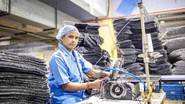 A focused female factory worker at a textile plant in India, working with an industrial sewing machine.