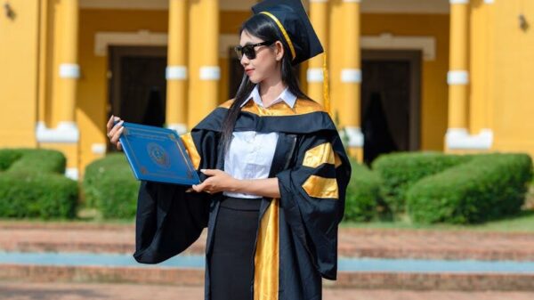 Graduate in cap and gown holding diploma outside historic yellow building.