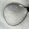 Detailed macro shot of white sugar crystals on a reflective spoon.