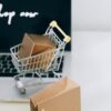 A miniature shopping cart with a parcel on a laptop symbolizes online shopping and e-commerce.