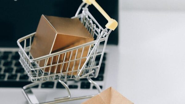 A miniature shopping cart with a parcel on a laptop symbolizes online shopping and e-commerce.