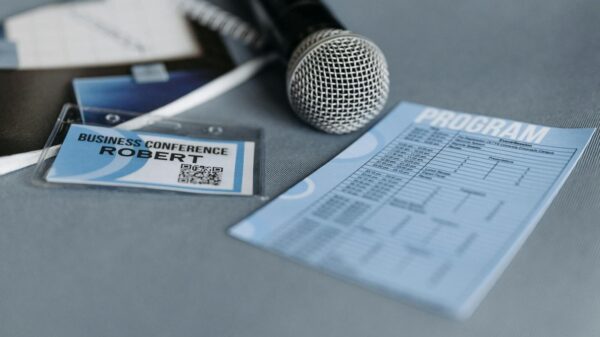 Close-up of a microphone, name tag, and program guide on a table at a business conference.