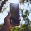 Close-up of hand holding smartphone with sunlight and blurred bokeh background, emphasizing technology in nature.