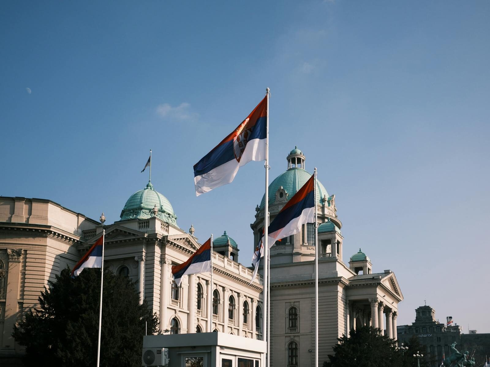 Serbian parliament building with national flags on a clear day.