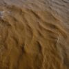 Aerial view of a muddy river with brown sediment, showcasing natural erosion and water movement.