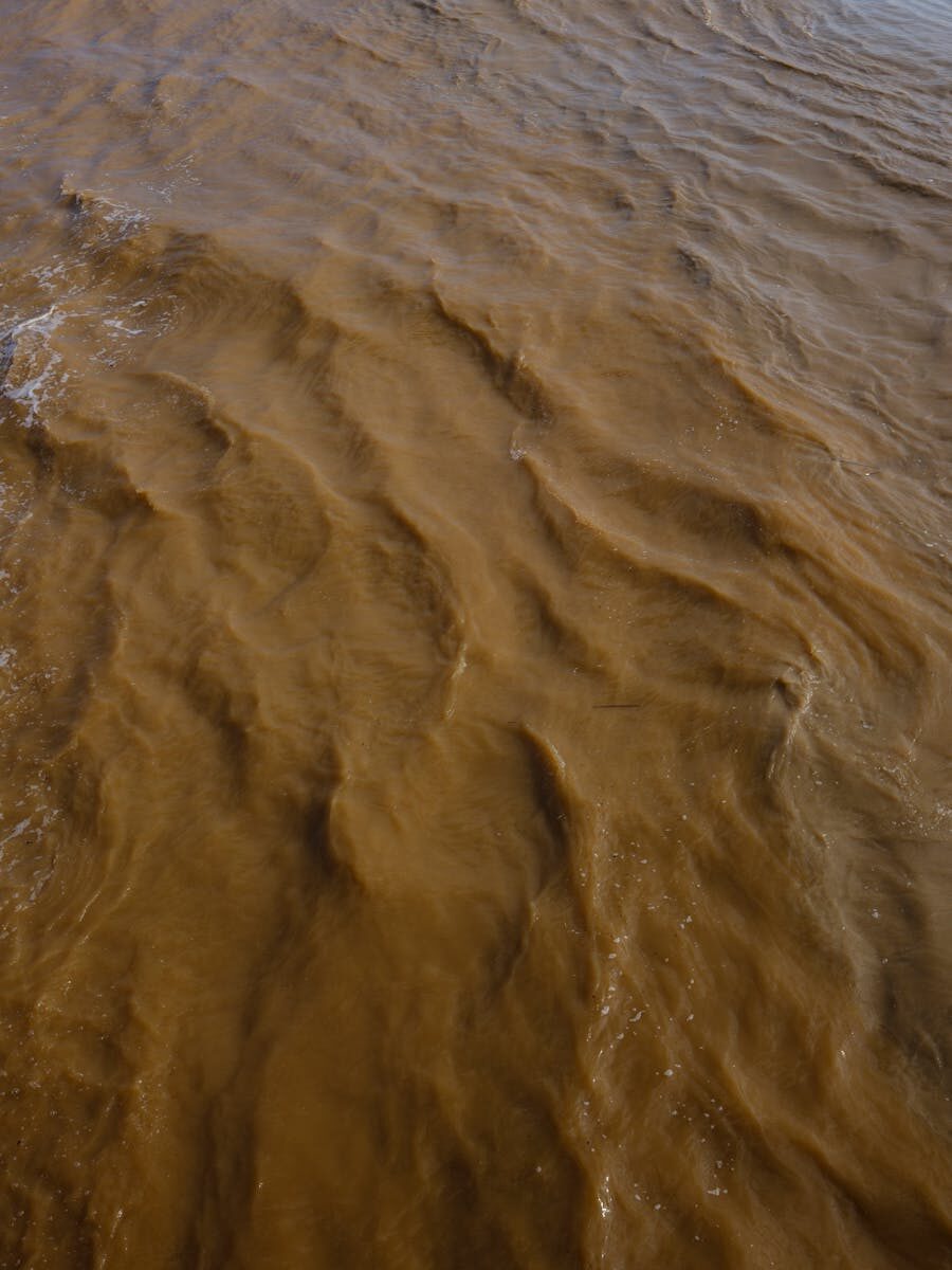Aerial view of a muddy river with brown sediment, showcasing natural erosion and water movement.
