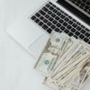 A stack of US dollar bills on a laptop keyboard representing online finance and budgeting.