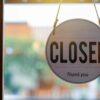 Wooden closed sign hanging on a shop window, with blurred background outside.