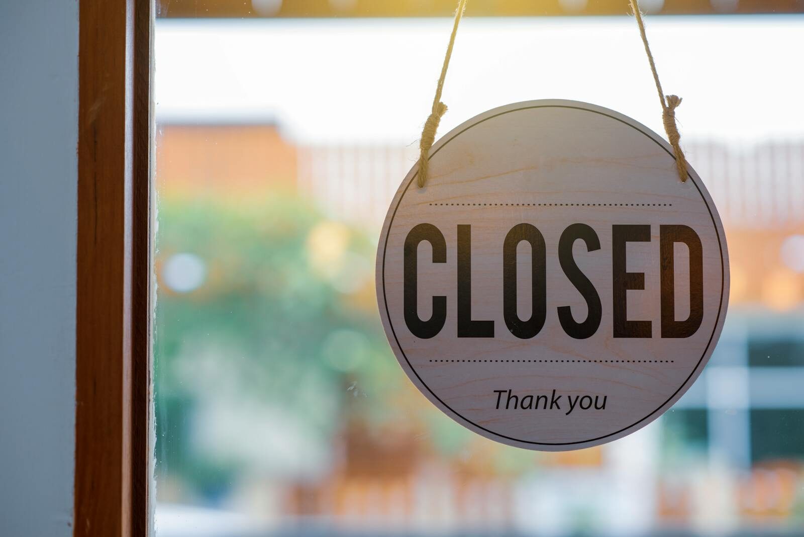 Wooden closed sign hanging on a shop window, with blurred background outside.