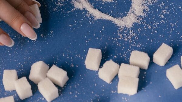 Top view of sugar cubes and a heart drawn in sugar on a blue surface with a hand nearby.