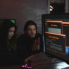 Cybersecurity experts in hoodies analyzing encrypted data on computer screens in an indoor setting.