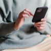 Crop faceless female in casual clothes using smartphone and touching screen while chilling at home
