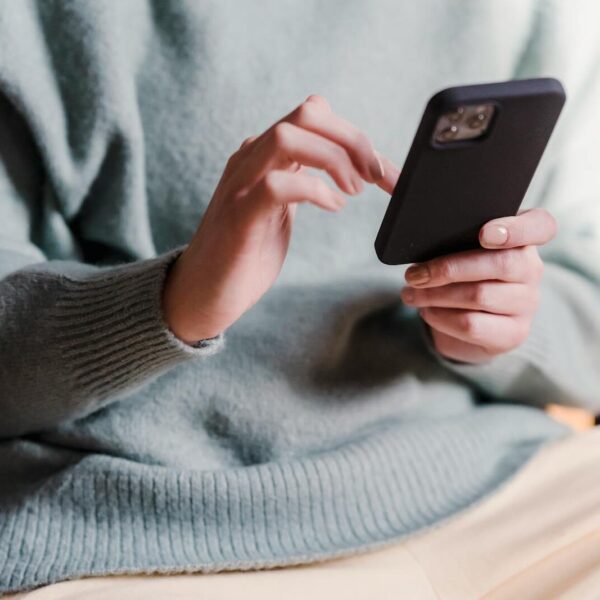 Crop faceless female in casual clothes using smartphone and touching screen while chilling at home