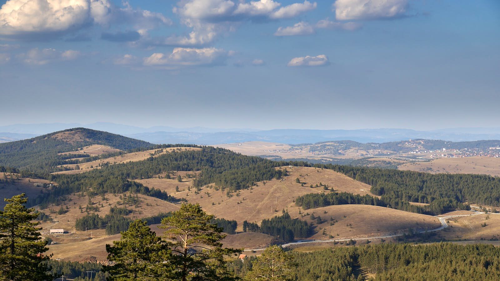Aerial view of the rolling hills and forests of Zlatibor, Serbia, under a clear sky.