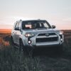 Silver Toyota SUV driving on a dirt road with sunset background, ideal for travel themes.