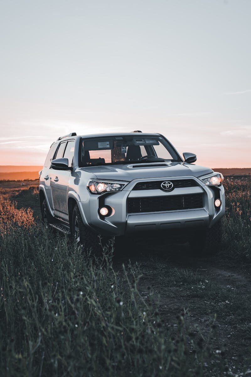 Silver Toyota SUV driving on a dirt road with sunset background, ideal for travel themes.