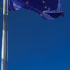 Close-up of the European Union flag fluttering on a flagpole against a deep blue sky.