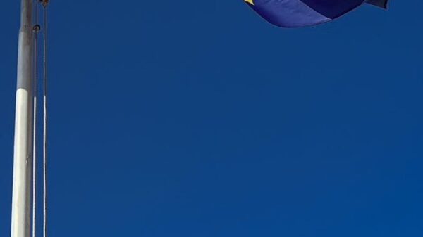 Close-up of the European Union flag fluttering on a flagpole against a deep blue sky.