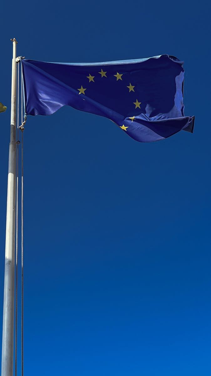 Close-up of the European Union flag fluttering on a flagpole against a deep blue sky.