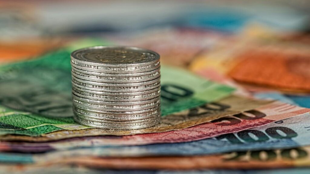 A stack of coins on top of various colored banknotes, symbolizing finance and currency.