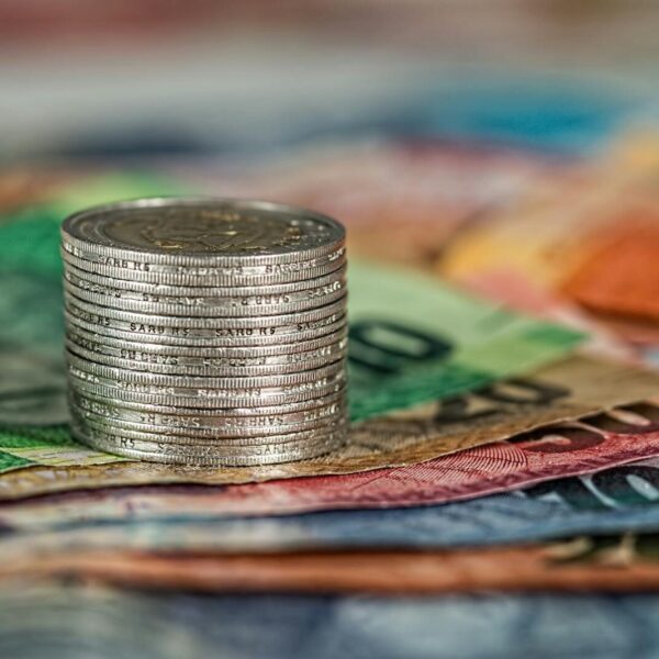 A stack of coins on top of various colored banknotes, symbolizing finance and currency.