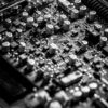 Detailed black and white close-up of an electronic circuit board with capacitors and transistors.
