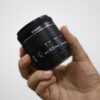 Detailed image of a hand holding a Canon camera lens indoors.