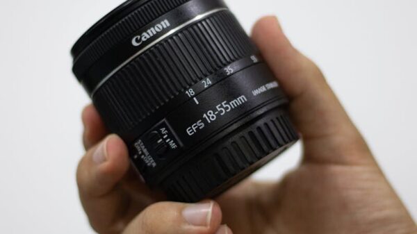 Detailed image of a hand holding a Canon camera lens indoors.