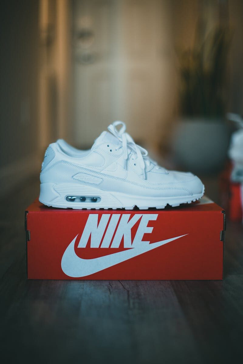 Stylish white sneaker displayed on a red Nike shoebox indoors. Perfect for fashion enthusiasts.