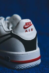 Detailed close-up of a white Nike Air Force 1 sneaker with red accents on a blue background.