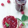 Delicious raspberry jam spread on toast with fresh raspberries on a white wooden background.