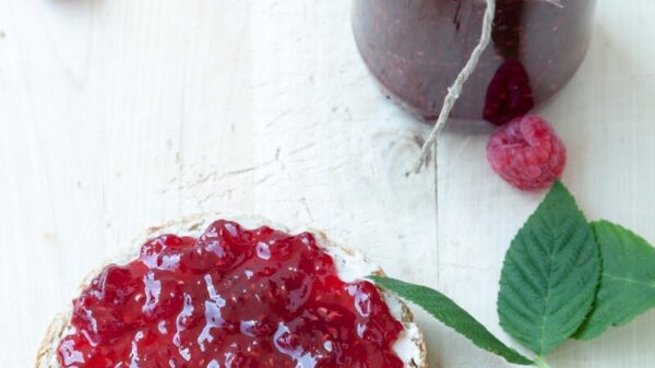 Delicious raspberry jam spread on toast with fresh raspberries on a white wooden background.