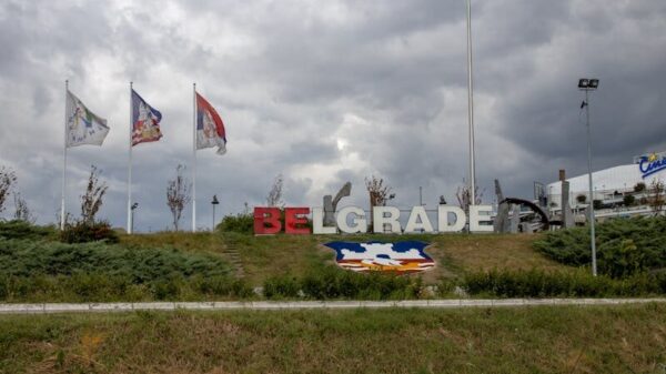 Belgrade sign with Serbian flags under dramatic overcast sky, capturing national pride.