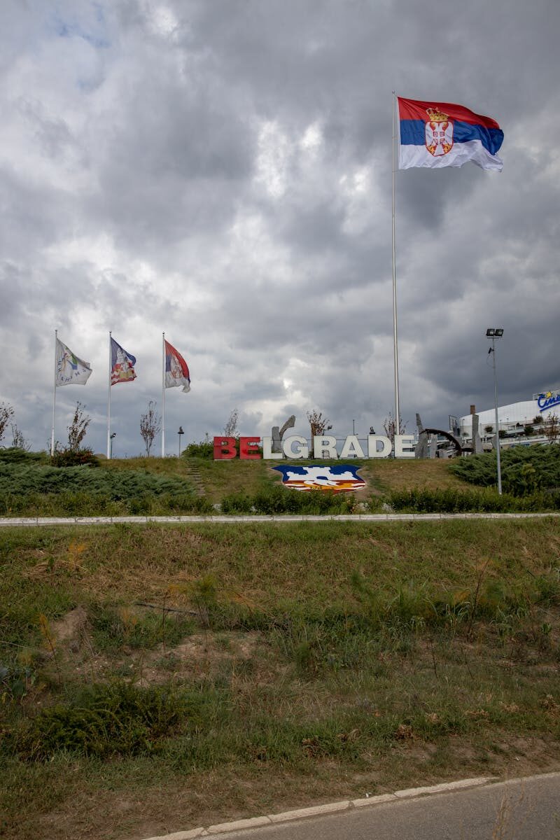 Belgrade sign with Serbian flags under dramatic overcast sky, capturing national pride.